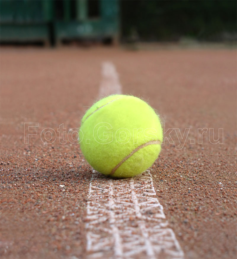 Теннисный мяч желтого цвета н агрунтовом корте